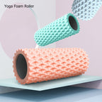 Two yoga foam rollers, one pink and one green, on a light blue surface with a pink background.