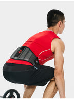 Person wearing a red sleeveless shirt and black shorts with a black back support device on a white background