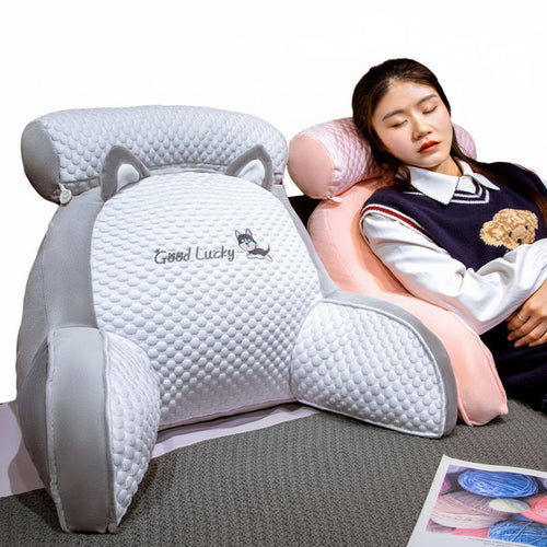 Person using a large white pillow with bear ears and 'Good Lucky' text, sitting on a bed.
